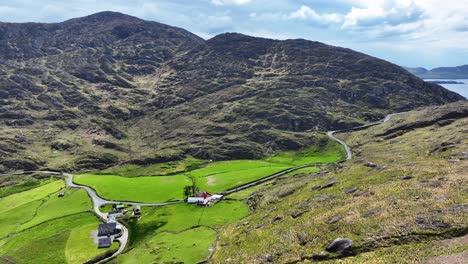 Drone-flying-to-road-pass-in-the-mountains-with-road-passing-farm-in-lush-green-fields,West-Cork-Ireland