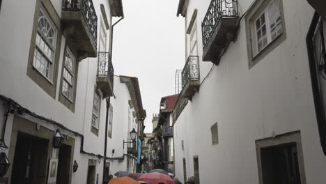 Weiße-Fassadenwand-Mit-Holzverkleideten-Fenstern-Und-Menschen,-Die-Mit-Regenschirmen-Spazieren-Gehen