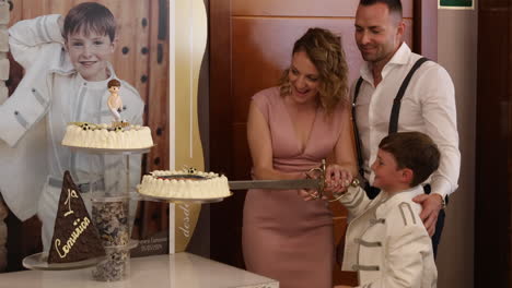 Un-Niño-Corta-Su-Pastel-De-Comunión-Con-Su-Familia-En-Una-Celebración-En-Zaragoza,-España.