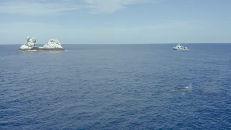 La-Ballena-Jorobada-Lanza-Aire-Con-Un-Barco-De-Buceo-Y-Las-Islas-Revillagigedo-Al-Fondo.