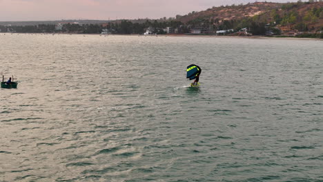 Windsurfista-En-Hidroplano-Tallando-Formas-En-Forma-De-&quot;s&quot;-Sobre-El-Agua-Con-Una-Audiencia-De-Una-Persona-Sentada-En-Un-Bote-Tipo-Cesta