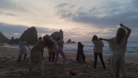 Glückliche-Frauen-Tanzen-Am-Strand-Mit-Großen-Klippen-Im-Hintergrund