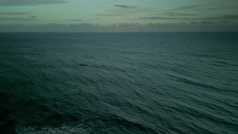 Wide-aerial-of-dramatic-wavy-Pacific-ocean-and-cloudy-horizon-at-dusk