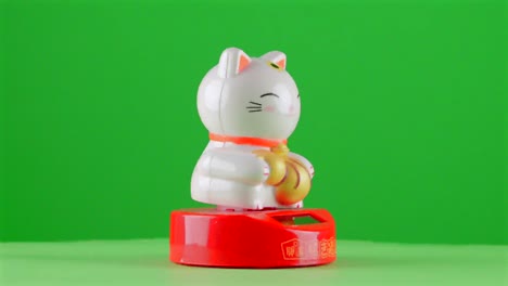 Maneki-Neko-Dinero-De-La-Suerte-Fortuna-Símbolo-Japonés-Recuerdo-Del-Gato-Inclinándose-Sobre-Fondo-Verde-Fondo-De-Clave-Cromática-Reemplazo-De-Fondo-Objeto-En-Un-Tocadiscos-Bucle-Giratorio-3d