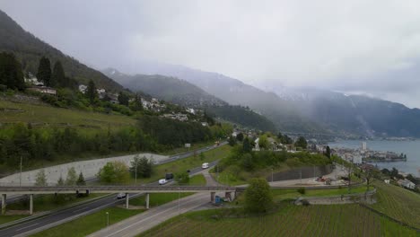 Following-aerial-shot-of-trucks-and-cars-on-highway-in-Switzerland-next-to-Lake-Geneva-with-mountains-in-the-background