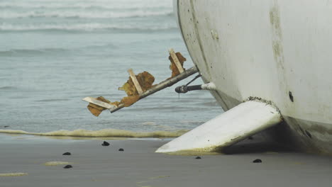 Olas-Corriendo-Por-El-Yate-Arrastrado-En-Una-Playa-Sombría---Primer-Plano-De-La-Quilla