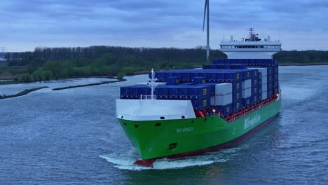 BG-Green-Containership-Vessel-With-Wind-Turbines-In-The-Background-Near-Barendrecht,-Netherlands