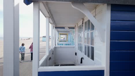 Blick-Durch-Eine-Reihe-Von-Hölzernen-Strandhütten-Am-Meer,-Während-Menschen-Vorbeigehen