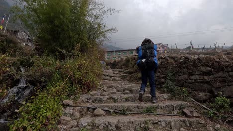 Man-carrying-a-heavy-backup-up-a-steep-staircase-entering-a-mountain-valley-in-the-himalayas-of-Nepal