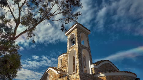 Campanario-E-Iglesia-De-Piedra-Con-Un-árbol-Bajo-Un-Cielo-Parcialmente-Nublado