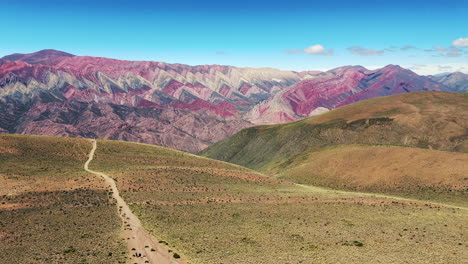 Drone-advances-over-a-path-as-tourists-journey-towards-the-Mirador-del-Cerro-de-los-14-Colores,-also-known-as-Hornocal