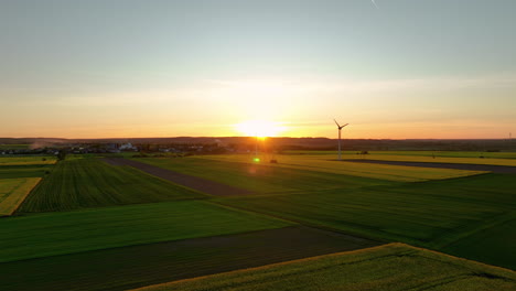 Aerial-view-of-green-and-yellow-fields-with-a-wind-turbine-at-sunset