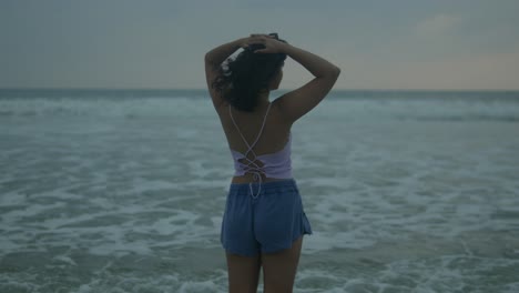 Woman-in-summer-attire-enjoying-serene-beach-at-dusk,-hair-tousled-by-gentle-breeze