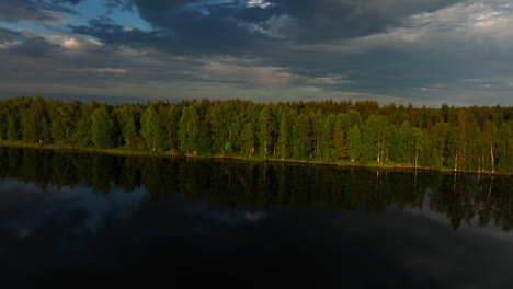AERIAL:-Mirroring-water,-arctic-Taiga-forest-and-a-cloudy-sunset-sky-in-Lapland