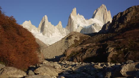 Zoom-in-perspective-from-a-river-bank-in-Patagonia,-Argentina-showcases-the-frozen-Mount-Fitz-Roy
