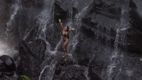 Eine-Frau-In-Einem-Schwarzen-Bikini-Steht-Auf-Den-Felsen-Unter-Dem-Herabstürzenden-Wasser-Am-Kanto-Lampo-Wasserfall-In-Bali