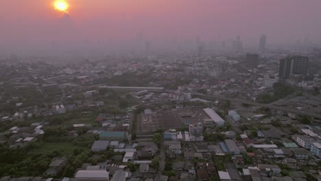 Aerial-view-of-buildings-and-houses-in-Bangkok-city,-with-a-stunning-sunset-amidst-fog