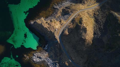 Top-down-view-of-vehicle-park-in-the-middle-by-the-road,-hills,-and-the-sea