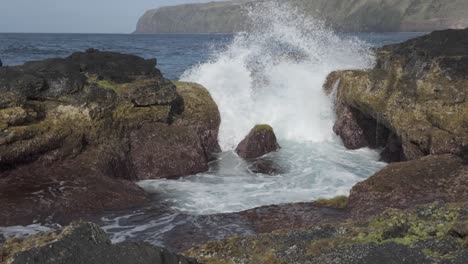 Wellen-Brechen-Gegen-Felsige-Klippen-Bei-Mosteiros,-Sao-Miguel-Mit-Einem-Entfernten-Hügel,-Lebendig-Und-Dynamisch