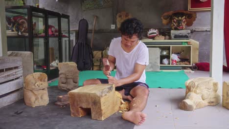 Asian-Wood-Carver-Working-On-Traditional-Barong-Mask-In-Bali,-Indonesia---Wide-Shot