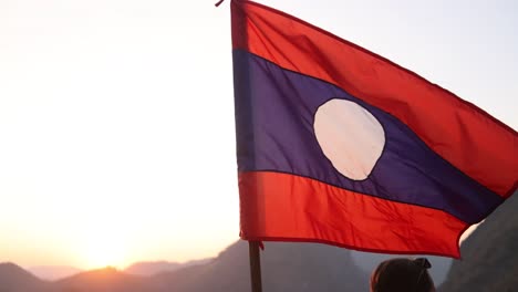 Laos-flag-flapping-in-the-wind-at-sunset-in-the-mountain-town-of-Nong-Khiaw-in-Laos,-Southeast-Asia