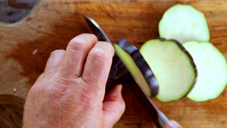 Overhead-view-of-male-caucasian-hands-using-knife-to-cut-aubergine-in-disks