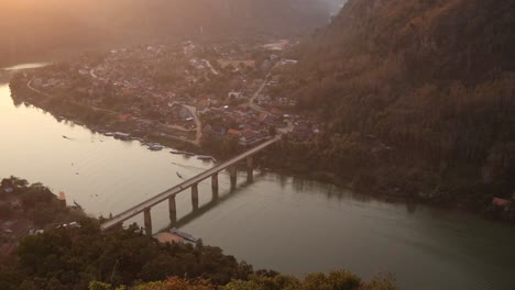 sun-setting-over-the-river-with-a-bridge-spanning-it-in-the-mountain-town-of-Nong-Khiaw-in-Laos,-Southeast-Asia