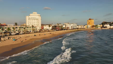 Aerial-tracking-shot-in-front-of-people-on-a-beach,-golden-hour-in-Mazatlan,-Mexico