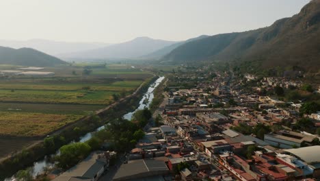 Contrasting-aerial-in-Tamazula-de-Gordiano's-housing-against-crop-fields,-separated-by-a-river