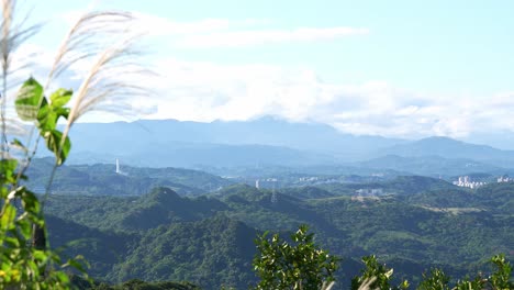 Una-Vista-Panorámica-De-Exuberantes-Colinas-Verdes-Y-Montañas-Distantes-Bajo-Un-Cielo-Azul-Claro,-Con-Algo-De-Vegetación-En-Primer-Plano,-Capturada-En-La-Antigua-Calle-Jiufen,-Distrito-De-Ruifang,-Nueva-Ciudad-De-Taipei,-Taiwán