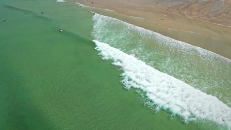 Fistral-Beach,-Draufsicht-Mit-Zeitlupe-Der-Wellen-Und-Surfer-Am-Strand,-Türkisfarbenes-Wasser-In-Cornwall,-Großbritannien