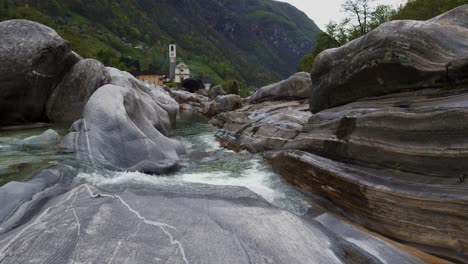 Pan-up-along-flowing-waters-smoothing-rocks-and-stones-to-chapel-in-Lavertezzo-Switzerland