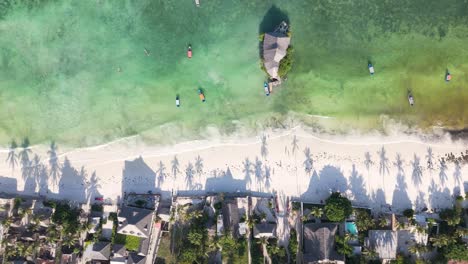 Drone-top-down-over-house-and-palm-shadow-by-turquoise-water-beach-in-sunset