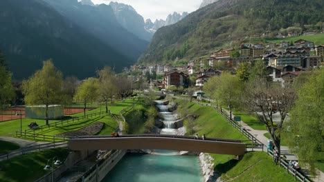 Pedestrian-bridge-crossing-stream-with-mountains-in-background,-Molveno-in-Italy