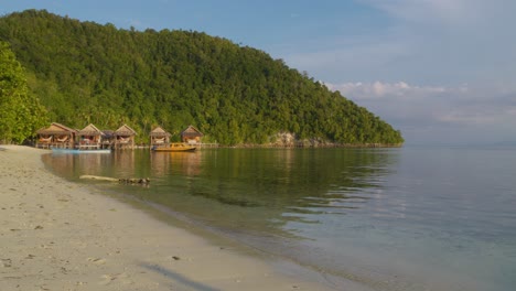 Ruhiger-Strand-Auf-Der-Insel-Kri-Im-Raja-Ampat-Archipel,-Indonesien,-Mit-Holzhütten-Entlang-Der-Küste-Vor-Einer-üppig-Grünen-Kulisse