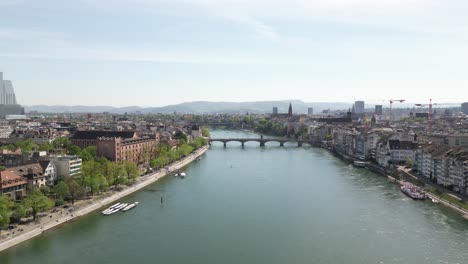 Aerial-drone-backward-moving-shot-over-Basel-medieval-old-town-along-both-sides-of-Rhine-river-in-Switzerland-at-daytime
