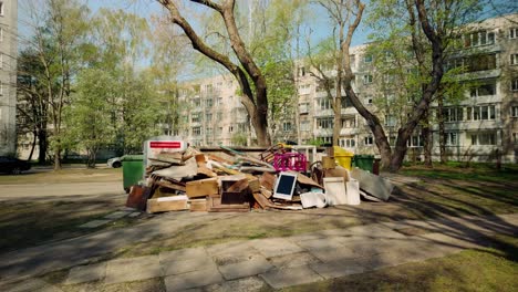 Muebles,-Basura-Y-Aparatos-Electrónicos-Tirados-Al-Suelo-Cerca-De-Contenedores-De-Basura-En-Un-Patio-De-Europa-Del-Este,-Punto-De-Vista-Hacia-Adelante.