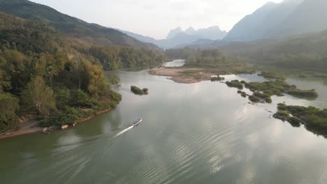 drone-shot-of-boat-going-down-the-river-in-the-mountain-town-of-Nong-Khiaw-in-Laos,-Southeast-Asia