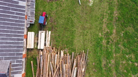 Preparing-wood-stacks-for-drying-near-farmstead-building,-aerial-top-down-view