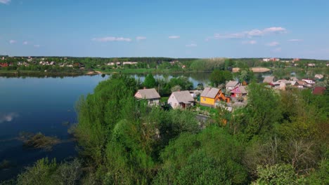 Grúa-De-Drones-Abajo-Con-Vistas-Al-Pueblo-Junto-Al-Río-Azul-Que-Termina-Con-Un-Paisaje-Rural-De-Primavera-En-Flor