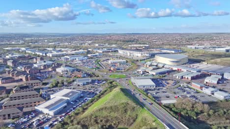 A-cinematic-shot-from-above-featuring-light-traffic-flowing-along-contemporary-warehouses,-parking,-a-shopping-mall-of-Derby,-England-on-calm-sunny-day