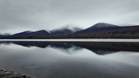 Slow-flow-of-another-half-of-the-frozen-river-against-the-background-of-a-gray-sky-and-snowy-mountains-4k