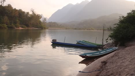 canoe-boats-docked-on-river-bank-in-the-mountain-town-of-Nong-Khiaw-in-Laos,-Southeast-Asia