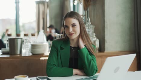 charming-woman-in-a-green-jacket-looks-at-the-camera-and-smiles-against-the-backdrop-of-a-beautiful-restaurant