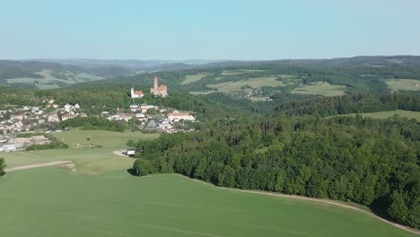 Vista-Aérea-Del-Majestuoso-Castillo-De-Bouzov-En-La-República-Checa,-Encaramado-En-Lo-Alto-De-Una-Colina-Y-Rodeado-De-Verdes-Bosques-Y-Un-Pintoresco-Pueblo.