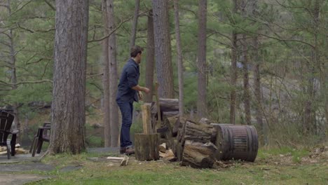 Mann-Hackt-Holz-Mit-Einer-Axt-Auf-Einer-Waldlichtung,-Umgeben-Von-Bäumen-Und-Einem-Stapel-Baumstämme