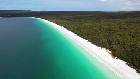 Video-De-Un-Dron-En-4k-Volando-Hacia-Atrás-Para-Revelar-Más-De-La-Impresionante-Playa-De-Hyams,-Una-Larga-Franja-De-Arena-Blanca-Con-Selva-Tropical-A-Un-Lado-Y-Aguas-Azules-Del-Océano-Al-Otro.