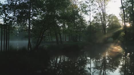 Morgendämmerung-An-Einem-Ruhigen-See,-Die-Morgensonne-Wirft-Sanfte-Strahlen-Durch-Den-Nebel-Und-Die-Bäume