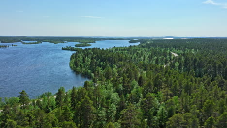 AERIAL:-Motorhome-driving-on-a-distant-road-at-lake-Inari,-summer-day-in-Finland