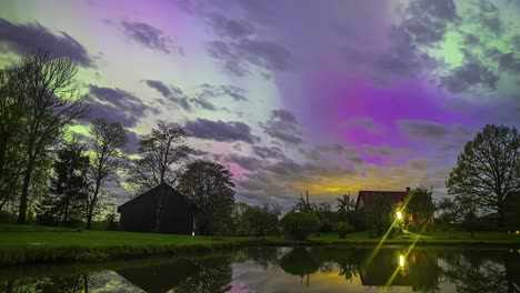 Aurora-borealis-shine-through-the-clouds-in-a-dreamy-time-lapse-above-a-countryside-cabin